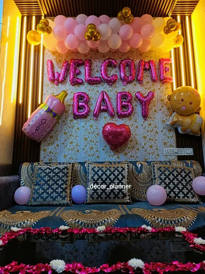 A closer look at the 'Welcome Baby' backdrop against a beautifully lit wall panel. The pink and gold balloons, along with baby-themed foil balloons, create a warm and celebratory focal point.
