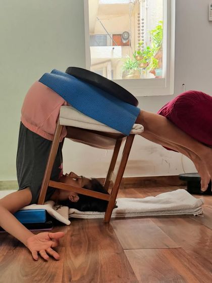 This supported Halasana (Plow Pose) uses a stool and weights. This therapeutic variation is excellent for athletes or anyone with tight hamstrings, as it allows the muscles to release passively while calming the nervous system.