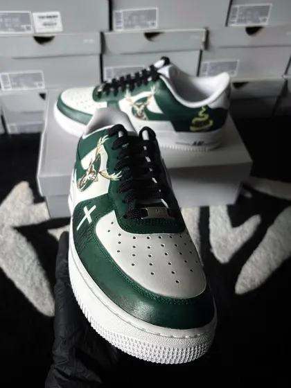 A front-facing shot of the Jägermeister-themed AF1s. This angle highlights the clean lines and detailed artwork on the front and side of the shoe, set against a background of fresh sneaker boxes.