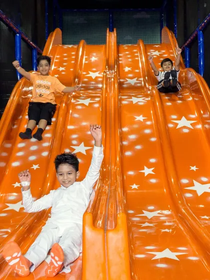 A group of excited kids coming down the big orange slide, hands in the air. This is one of the most thrilling experiences in My Maze.