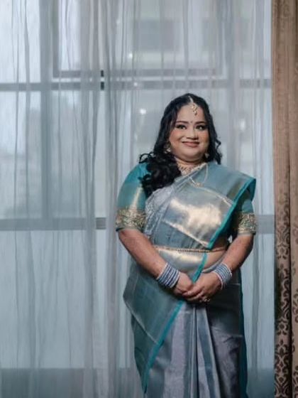 A full-length view against a window, showcasing the beautiful sheen of the saree and the bride's graceful posture.