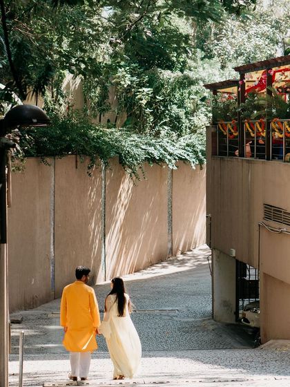 A couple in traditional yellow and white outfits walks away hand-in-hand, symbolizing their journey forward together.