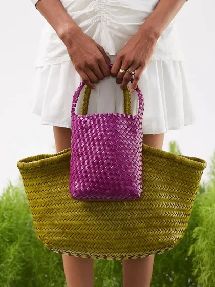 Big and small, our handwoven bags come in all sizes. Here, the vibrant purple Axel Mini is held against the olive green Axel Large, showcasing the range of colors and sizes in our Summer '24 collection.