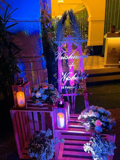 The welcome area for an engagement, featuring a personalized sign, wooden crates, and lanterns. The purple uplighting adds a touch of modern drama.