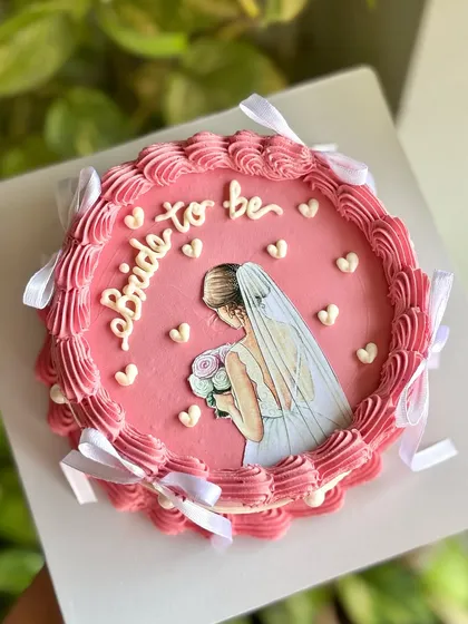 A top-down view of the bride-to-be cake, highlighting the central illustration and the beautiful border of piped buttercream and bows.