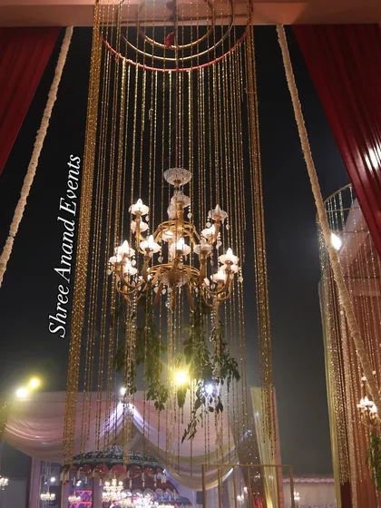 A magnificent hanging chandelier, adorned with greenery and surrounded by a cascade of golden strings, creating a stunning light fixture.