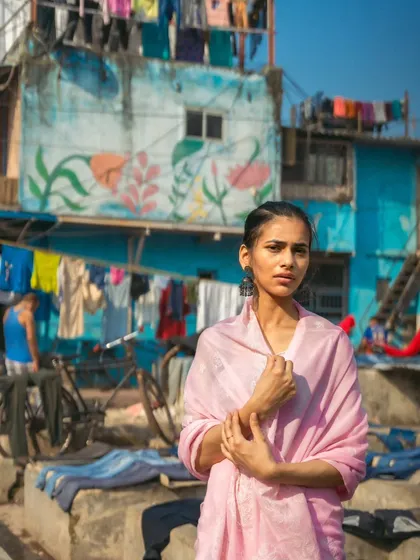 A full-body portrait at Dhobi Ghat, with the famous lines of laundry and colorful buildings creating a uniquely Mumbai backdrop.