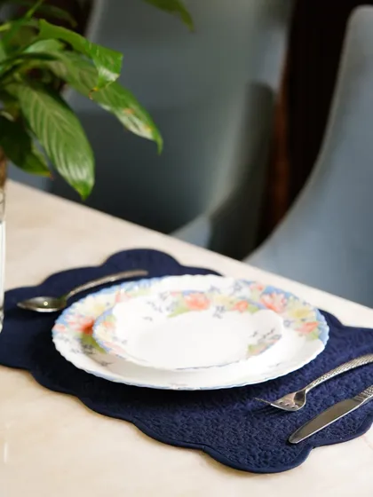 A scalloped navy blue placemat styled with floral dinnerware. The deep blue color provides a beautiful contrast, creating a sophisticated and classic table setting.