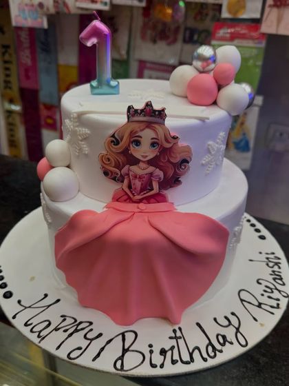 A princess doll cake for a first birthday. This two-tier cake features a beautiful princess topper with a flowing fondant dress, making it a fairytale centerpiece for a special celebration.
