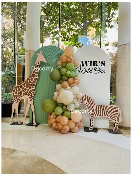 A simple and chic jungle safari photo booth with giraffe and zebra cutouts against a backdrop of green and beige.
