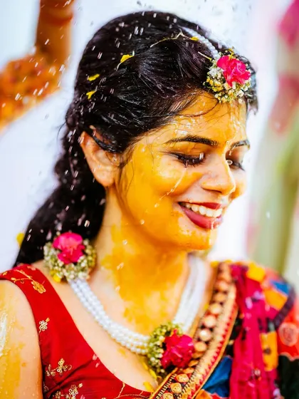 A candid shot of the bride's joyful reaction during her Haldi ceremony, covered in turmeric and flowers.