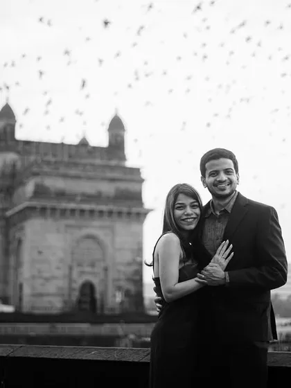 A joyful black and white portrait in front of the Gateway of India, with a flock of birds adding a dynamic and magical element to the scene.