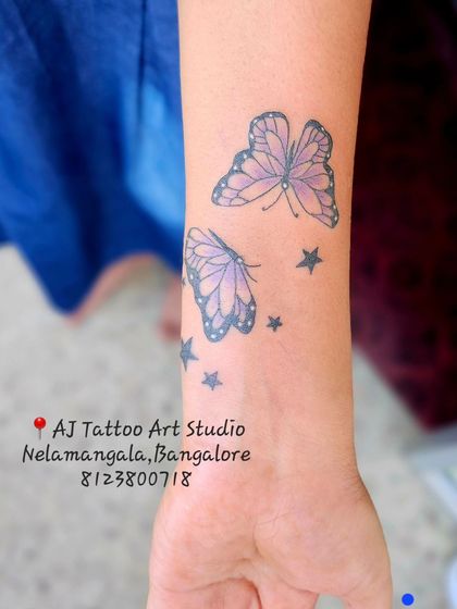 Two delicate purple butterflies with stars, a beautiful and feminine wrist tattoo.