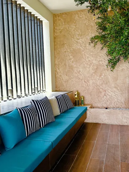 The vibrant blue of the bench cushions contrasts beautifully with the warm, earthy tones of the textured wall and wooden floor on this balcony.