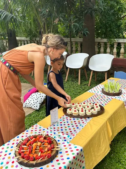 A mother and daughter picking out treats from the colorful food table. I design my kids' party spreads to be visually exciting, with items like fruit skewers and mini sandwiches.