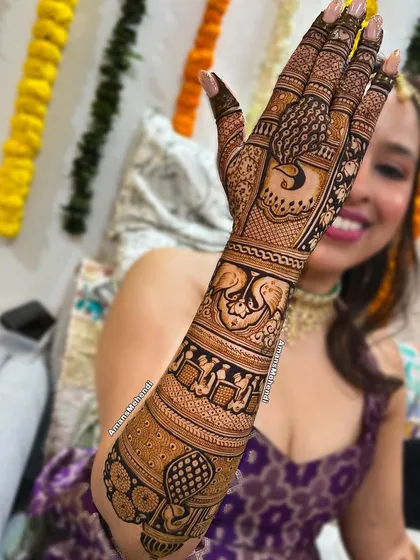 A happy bride showing her full-arm mehendi. This design features a variety of traditional elements like peacocks, swans, and intricate filler patterns.