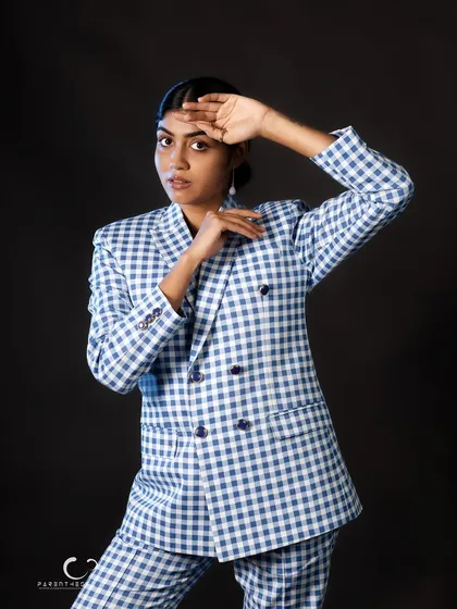 A more posed, fashion-oriented shot that highlights the structure of the suit. The hand gestures frame her face, drawing attention to her calm expression.