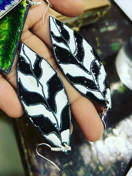 A close-up of the handcrafted enamel earrings, showing the glossy finish and the handmade silver hooks.