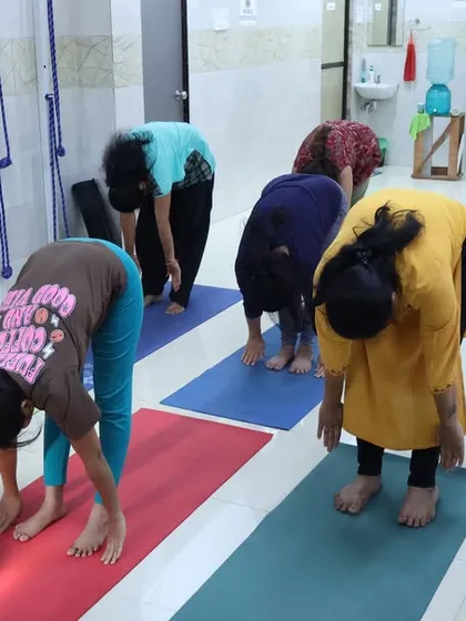 Students practice Padahastasana (Hand Under Foot Pose) during our in-person yoga camp. This deep forward bend stretches the hamstrings and spine while calming the mind.