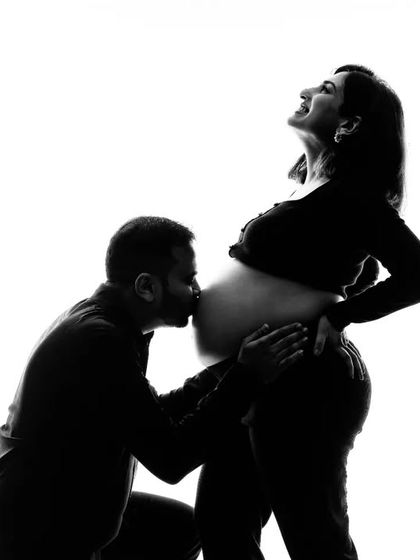 A classic black and white silhouette showing a partner's tender kiss on the baby bump. This is a deeply emotional and artistic shot that many of our clients cherish.