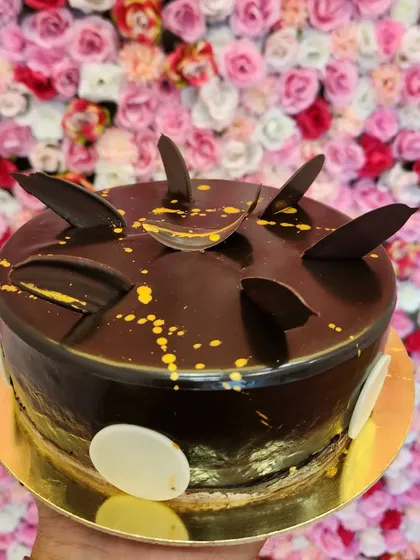 Another take on the Choco Maddy cake, this one is decorated with abstract chocolate pieces and splatters of edible gold paint. It's a modern and artistic design for a delicious chocolate cake.