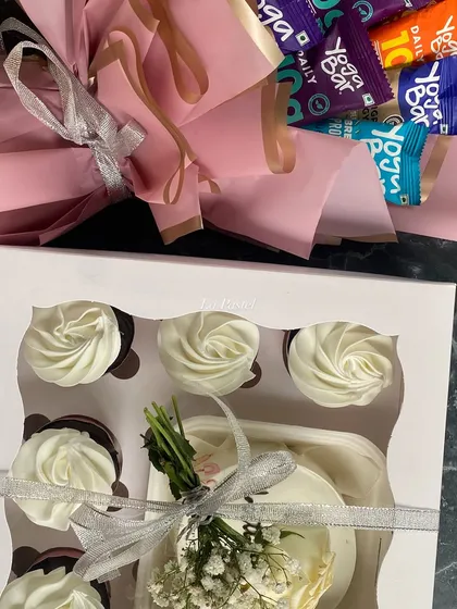 A top-down view of the sweet and savory hamper, showing the neatly arranged cupcakes and the colorful bouquet of protein bars.