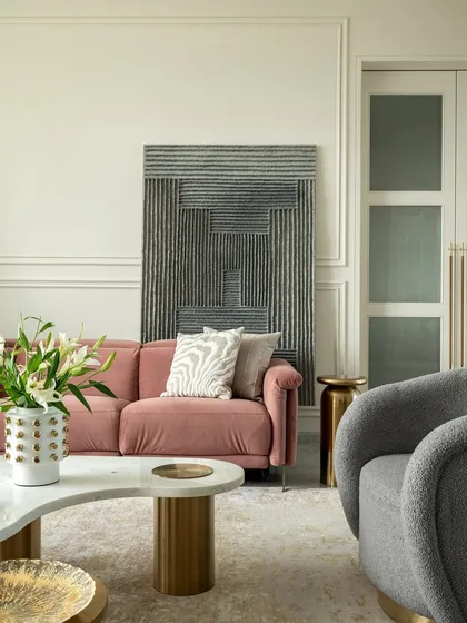The living room setup is designed for comfort and style. The pink sofa is complemented by a textured gray armchair and a unique marble coffee table with brass legs, creating a harmonious and sophisticated look.