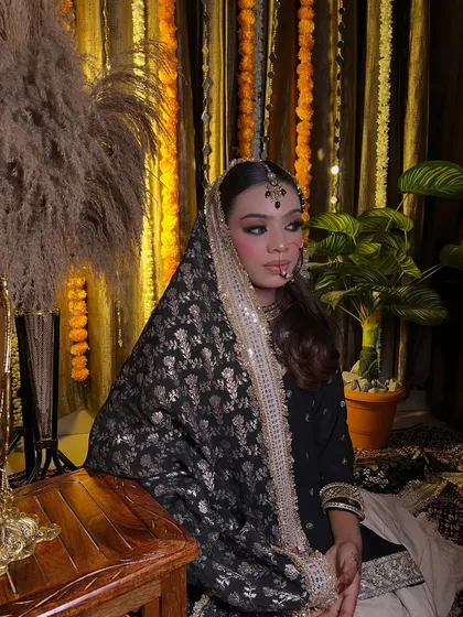 A full portrait of a bride in a traditional black and gold outfit. The setting with marigold flowers adds a festive touch to this unique look.