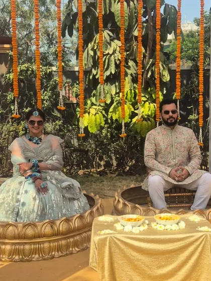 A grand Haldi ceremony setup. The bride and groom look perfect, with the bride wearing a unique blue floral set that stands out against the traditional yellow decor.