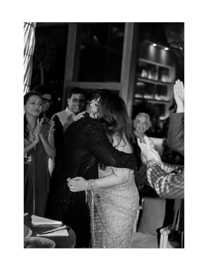 A beautiful black and white photo of a celebratory hug at Juhi and Jay's engagement party, surrounded by the happy faces of their loved ones.