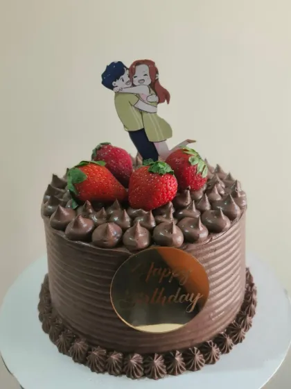 A decadent chocolate birthday cake topped with fresh strawberries and a cute couple topper.