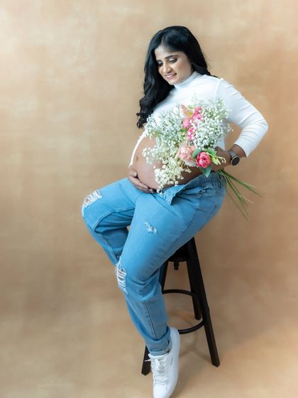 A modern and casual studio portrait of a mom-to-be in ripped jeans, cradling her baby bump and a bouquet of flowers.