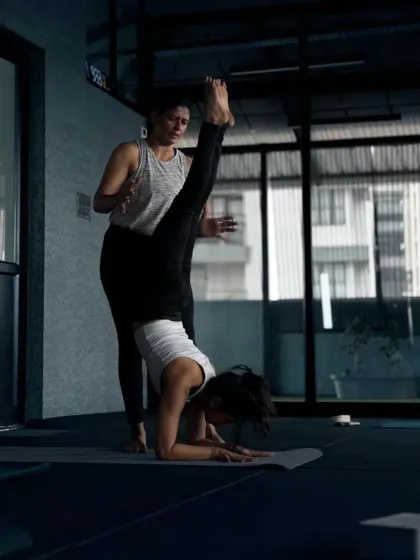 This is a moment of trust and focus in our advanced workshop. I'm guiding a student through a split-leg variation of Pincha Mayurasana, helping her find the balance between strength and flexibility.