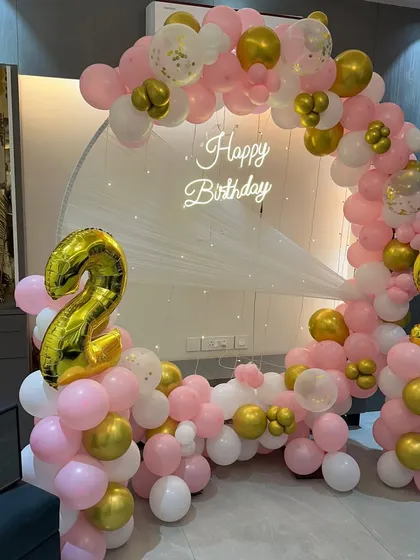 A lovely pink, white, and gold balloon ring for a 29th birthday. The setup includes large foil number balloons and a "Happy Birthday" neon sign.