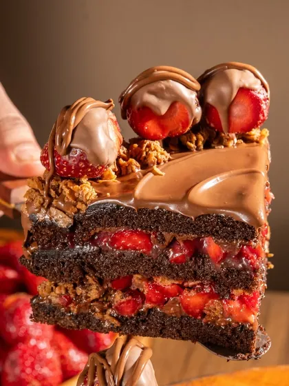A slice of our Crunchy Crumble Nutella Strawberry cake held up to show the incredible texture. You can see the crumble mixed right into the layers with the compote and Nutella.