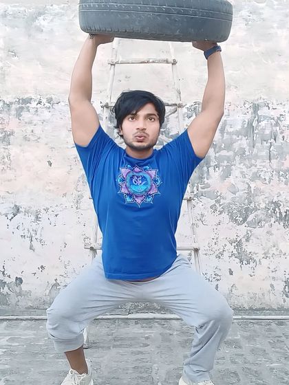 Demonstrating a tire overhead squat. I teach my online clients how to use their surroundings to get a powerful workout.