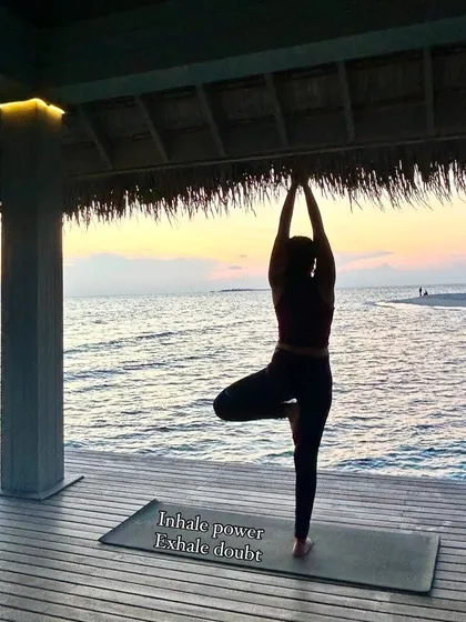 Finding stillness in Vrikshasana, the Tree Pose, as the sun sets. This pose is all about balance, focus, and rooting down to feel stable. The message on my mat, "Inhale power, Exhale doubt," is a core part of my teaching, focusing on breathwork to build mental and physical strength.