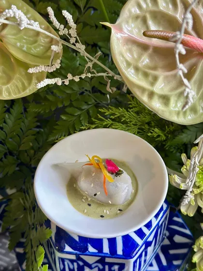 A Thai Basil Dumpling resting in a flavourful green curry dressing, garnished with delicate vegetable slivers. A taste of Southeast Asia in one perfect bite.