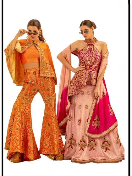 A studio lookbook image for Nighat Izhar Designs, featuring two models in modern Indian fusion wear. The clean white background and confident poses highlight the bold colors and contemporary silhouettes of the outfits.