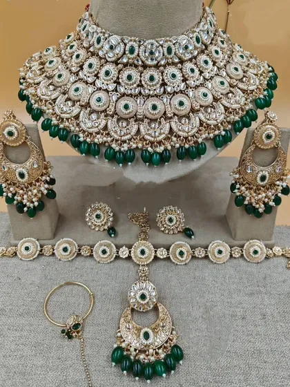 This is a complete Sabyasachi-inspired bridal jewellery set in emerald green. The set includes a heavy choker, matching oversized chandbali earrings, a mathapatti, a nath, and hathphool, all available for rent.