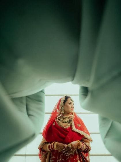 A creative shot of the bride in her red lehenga, framed by the groom's sherwani.