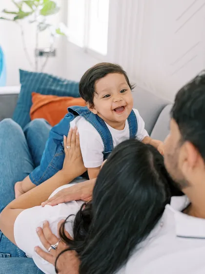 A playful moment on the couch, with the baby laughing as his parents look on. Genuine joy is the best ingredient for a photo.
