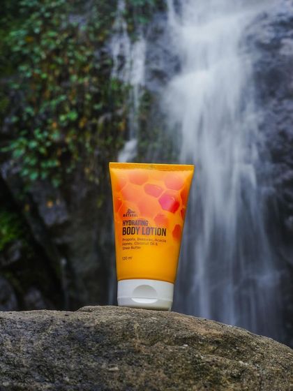 A beautiful outdoor shot of a hydrating body lotion placed on a rock with a waterfall in the background. The slow shutter speed creates a silky water effect, adding a touch of magic.