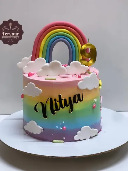 A vibrant rainbow theme cake for a 9th birthday. This chocolate truffle cake features a beautiful rainbow gradient made with whipped cream, topped with a fondant rainbow and clouds.