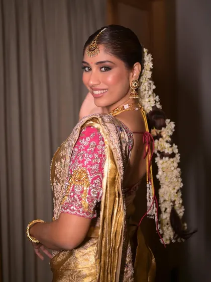 A beautiful back profile of a South Indian bride, showcasing the traditional Malinga flower braid. The makeup is kept soft and minimal to let the intricate details of her hair and saree shine.