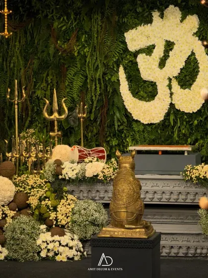 The heart of the celebration. The main altar features a floral 'Om' symbol, a golden Mooshak statue, and an abundance of fresh flowers against a living wall of greenery.