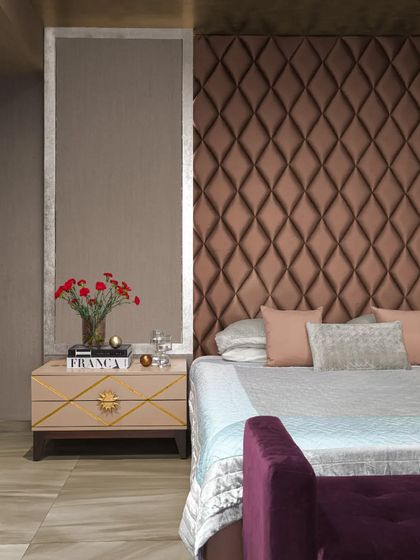 We designed this bold bedroom in the 'DLH' project using rich colors and textures to reflect dual personalities. A muted gold ceiling and a bronze, diamond-patterned headboard create a sense of drama, softened by mauve and pastel accents for a touch of understated opulence.