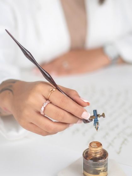 A close-up shot of me at my desk, dipping my calligraphy pen into a pot of golden ink. This image captures the focus and intention behind the art form, a moment of quiet before the writing begins. It's a practice of believing in your own potential.