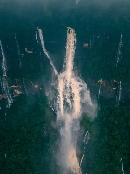 An aerial shot of Nohkalikai Falls, appearing like a brushstroke of white against the deep green canvas of Meghalaya's forests.