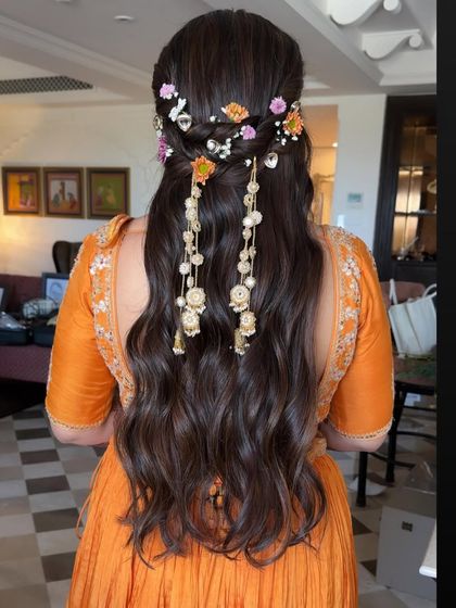 A beautiful half-updo with a braided crown and cascading floral and pearl accessories. This is an intricate and romantic style, perfect for a Haldi or Mehendi ceremony.
